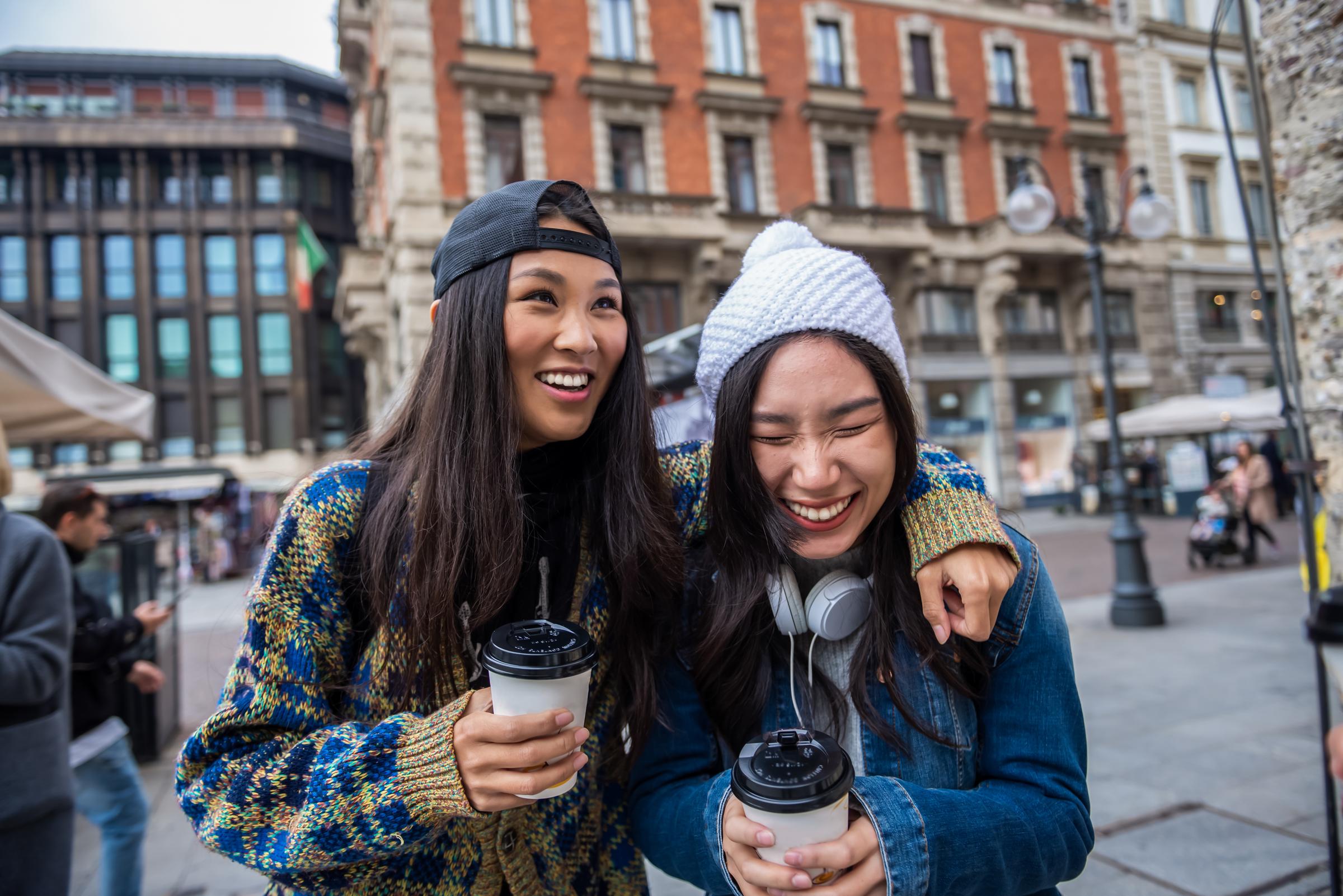Two young happy women walking with take away coffee in hands