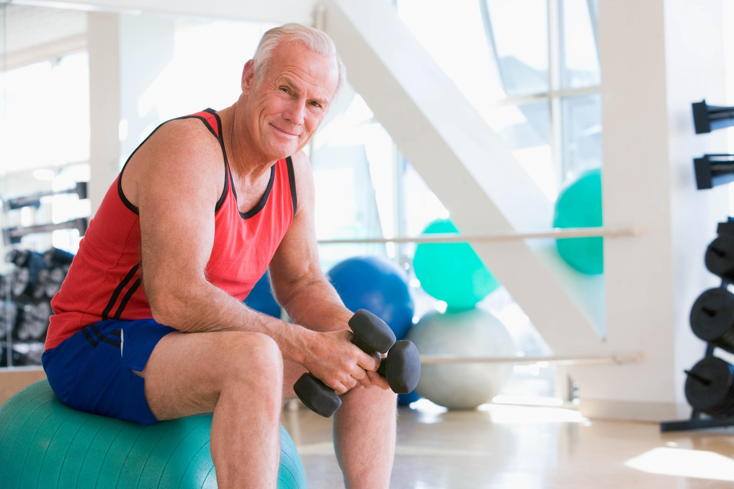 Man Using Hand Weights On Swiss Ball At Gym