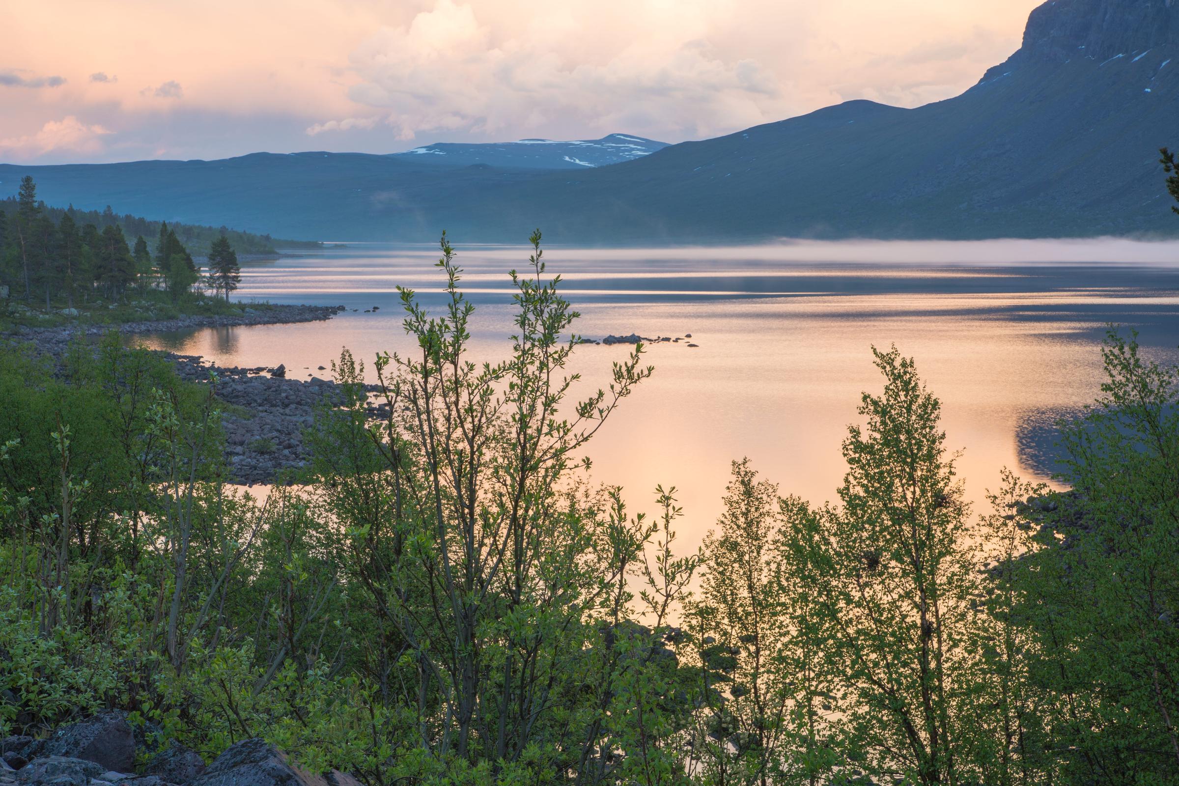 Dawn at stora sjöfallets national park with sun reflecting in the water and mountains in the background in Gällivare swedish lapland, Sweden
