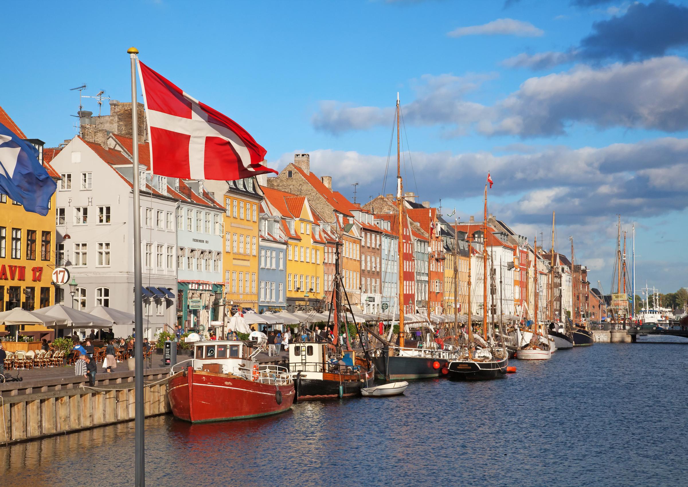Mennesker nyter solrike været i åpne kafeer av den berømte Nyhavn promenade